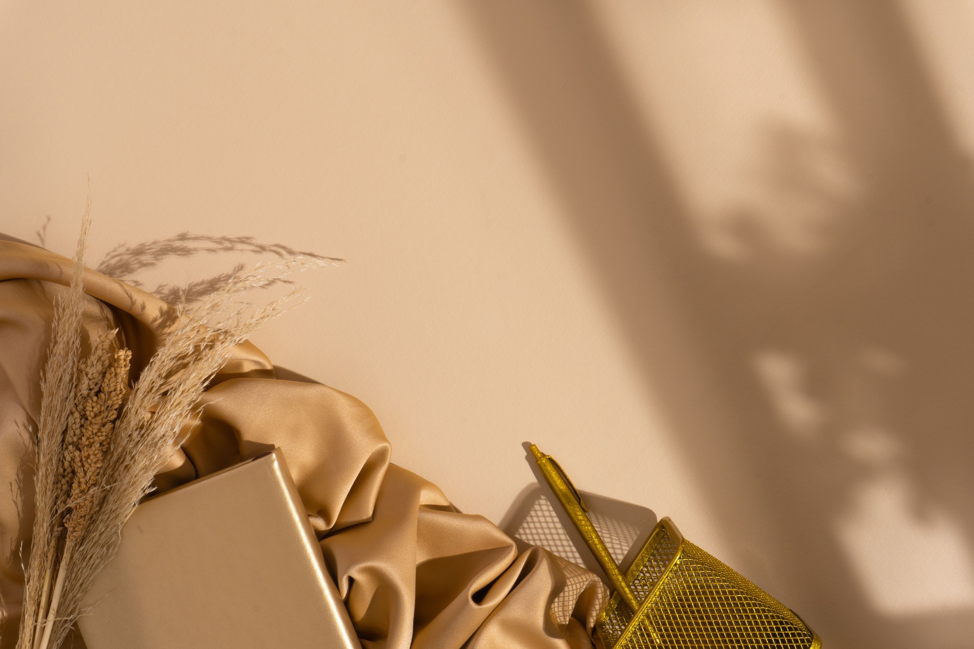 Autumn concept office desk with a pen, a notebook, a bundle of dried flowers, pen holder, a scarf and shadows on top of pastel brown background