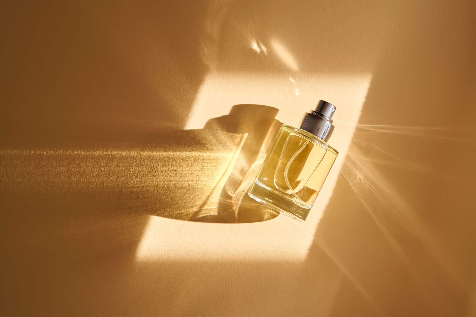 Perfume on a beige background in the rays of bright sun with beautiful highlights.