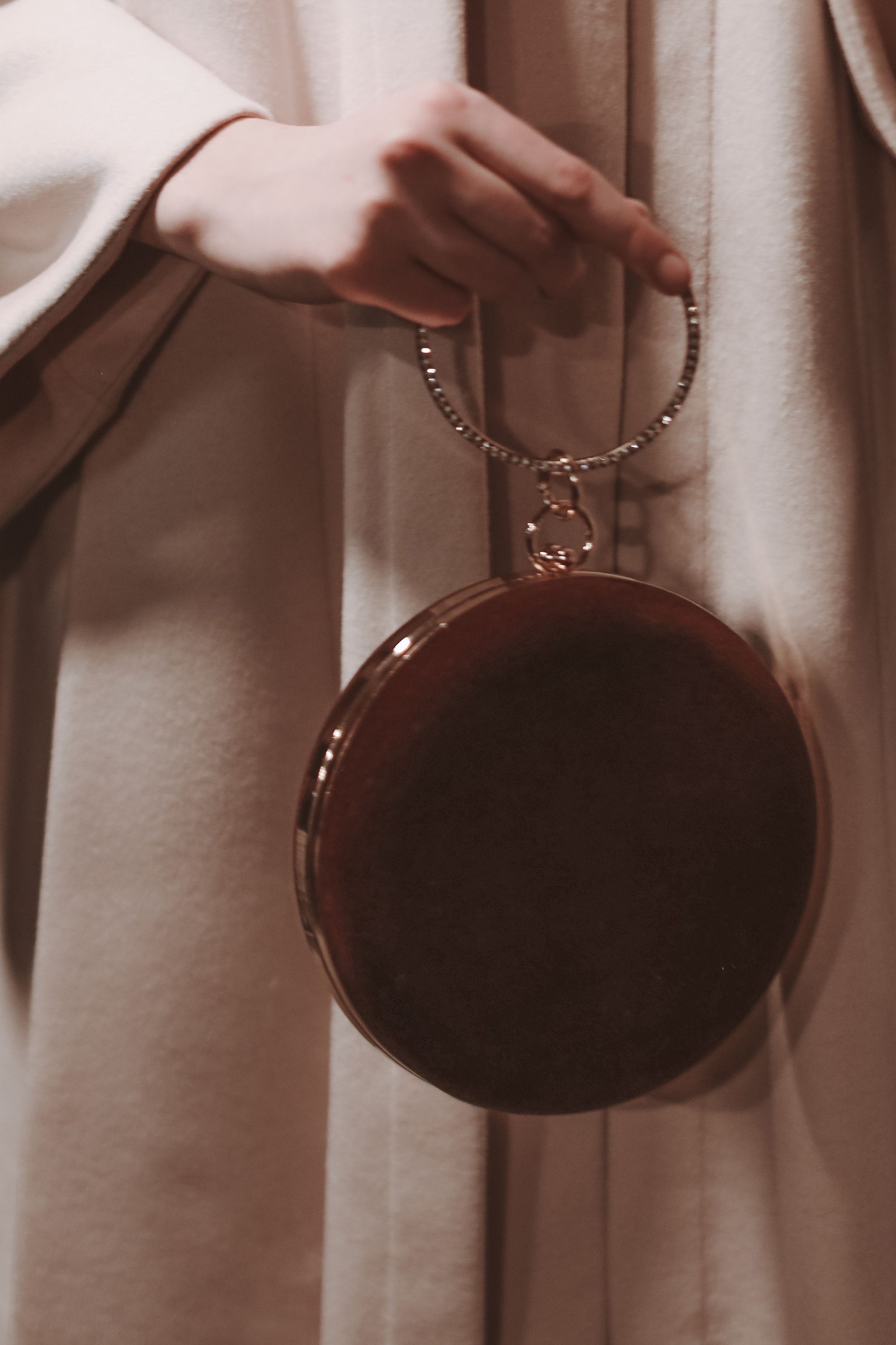 Female fashion details of beige coat and tiny velvet handbag or clutch with golden handle